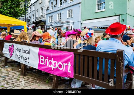 Bridport, Dorset. Inghilterra. Le persone celebrano il Bridport Hat Festival con copricapi fantasiosi e colorati. Musica dal vivo a Bucky Do Square. Foto Stock