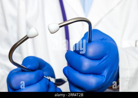 Primo piano estremo delle mani di un medico irriconoscibile che indossa guanti blu che reggono gli auricolari di uno stetoscopio. Foto Stock