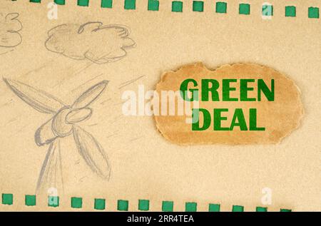 Un generatore eolico e le nuvole sono disegnate su cartone con fori verdi, accanto ad esso si trova un cartone con l'iscrizione Green Deal. Concetto ecologico Foto Stock