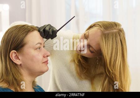 Il master disegna la forma delle sopracciglia con vernice bianca prima della correzione delle sopracciglia. Industria della bellezza. Foto Stock