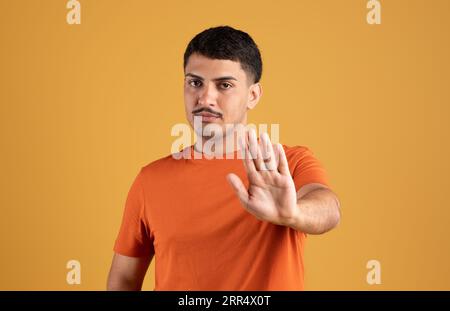 Rifiuto. L'uomo brasiliano scontento che gestisce si ferma con la mano, disapprova e rifiuta la cattiva offerta, sfondo giallo Foto Stock