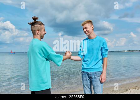I giovani amici si salutano quando si incontrano, stringono la mano, all'aperto Foto Stock