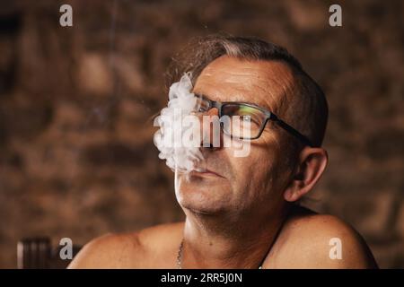 Un uomo anziano soddisfatto, sessant'anni, fuma con cura. Foto Stock