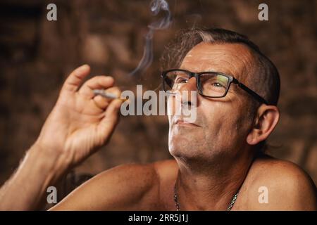 Un uomo anziano soddisfatto, sessant'anni, fuma con cura. Foto Stock