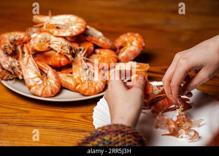 Grandi gamberoni cotti sul tavolo. Un uomo irriconoscibile sta mangiando gamberi a tavola. Foto Stock