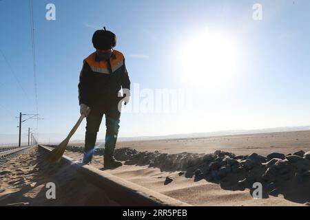 210113 -- AKSAY, 13 gennaio 2021 -- Un operaio ferroviario pulisce la sabbia nella contea autonoma di Kazak di Aksay nella provincia del Gansu della Cina nordoccidentale, 12 gennaio 2021. La ferrovia Dunhuang, che aprì completamente nel dicembre 2019, interseca le ferrovie esistenti, tra cui la ferrovia Lanzhou-Qinghai, la ferrovia Qinghai-Tibet e la ferrovia Lanzhou-Xinjiang, per formare la prima rete ferroviaria circolare nella regione nord-occidentale. Tra questi, la sezione da Yangguan a Shashangou si trova a Shazaoyuan, un luogo noto per il suo forte vento trasversale nella contea autonoma di Kazak di Aksay. La sabbia seppellirebbe la pista da tempo Foto Stock