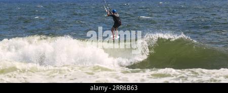 Vista posteriore di un Kitesurfer maschio che cavalca onde infranti nell'oceano al largo della costa di Long Island New York. Foto Stock