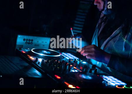 Primo piano delle mani dei DJ che suonano vari controlli dei brani sulla console di mixaggio dei DJ durante la festa del nightclub. Foto Stock