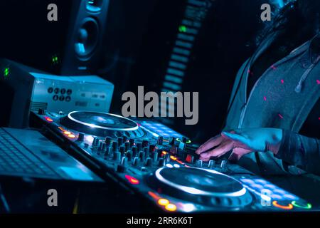 Primo piano delle mani dei DJ che suonano vari controlli dei brani sulla console di mixaggio dei DJ durante la festa del nightclub. Foto Stock