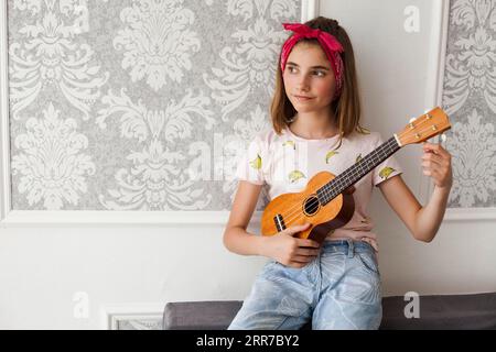 Ragazza sorridente seduta su un divano che regola il pensiero ukulele Foto Stock