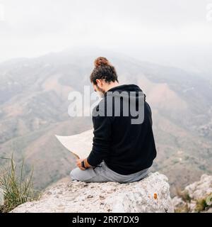 Un escursionista di sesso maschile seduto in cima alla cartina con l'aspetto roccioso Foto Stock