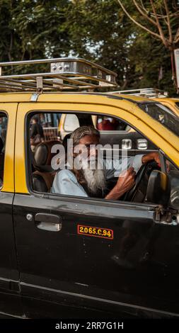 Vecchio tassista indiano seduto nel suo taxi, bloccato nel traffico a Mumbai, India. Foto Stock