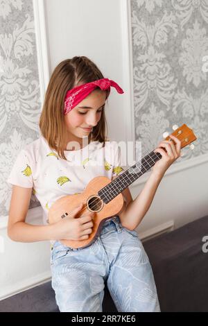 Bambina sorridente che gioca a casa ukulele Foto Stock