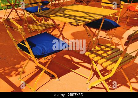 terrazza in legno di forma quadrata gialla e tavolo del ristorante. patio e terrazza. cuscino blu. forte contrasto. sedia pieghevole in legno e metallo. street cafe Foto Stock
