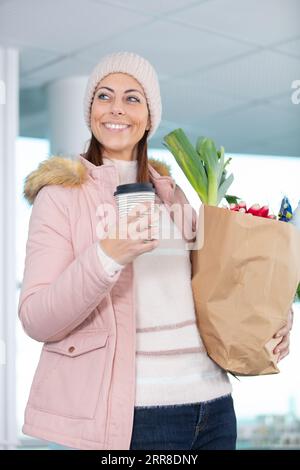 donna sorridente che tiene una tazza di caffè e generi alimentari in un sacchetto di carta Foto Stock