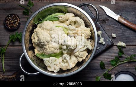 Cavolfiore fresco e organico in una ciotola di metallo, su un tagliere di legno e su uno sfondo di legno Foto Stock