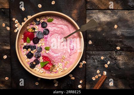 Farinata d'avena con noci, fragole e mirtilli con foglie di menta in un recipiente di ceramica. La ciotola è in piedi su un tavolo di legno Foto Stock