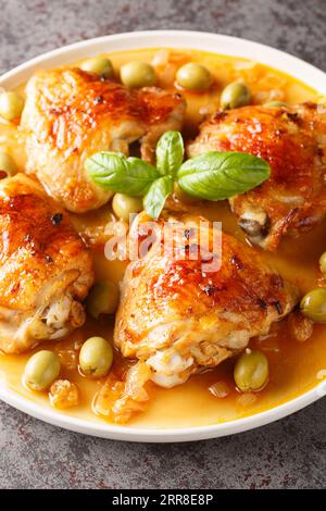 Deliziosa coscia di pollo cotta al forno con olive e salsa di cipolla da vicino in un piatto sul tavolo. Verticale Foto Stock
