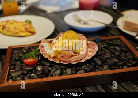 Uova alla Benedict con vongole decorative e ciottoli neri Foto Stock