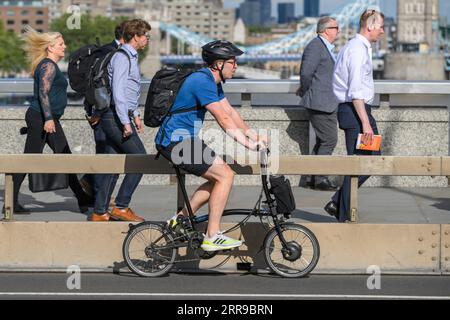 Un uomo che guida una bicicletta elettrica Brompton pieghevole attraverso il London Bridge, Londra, Regno Unito. 17 luglio 2023 Foto Stock