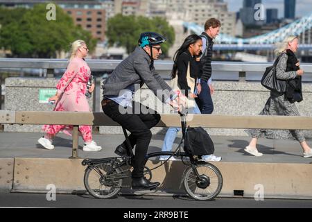 Un uomo che guida una bicicletta elettrica Brompton pieghevole attraverso il London Bridge, Londra, Regno Unito. 17 luglio 2023 Foto Stock
