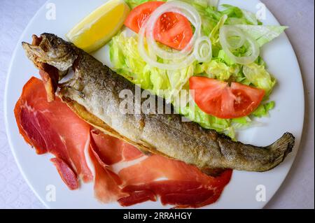 Piatto principale nel ristorante Asturiano, pesce trota intero alla griglia dal fiume di montagna servito con insalata mista fresca e pancetta Foto Stock