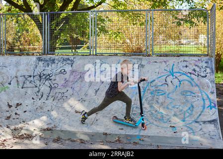 Bambino su kick scooter nel parco. I ragazzi imparano a rullo di skate board. Little Boy pattinaggio sulla soleggiata giornata estiva. Attività all'aperto per i bambini sulla sicurezza residen Foto Stock