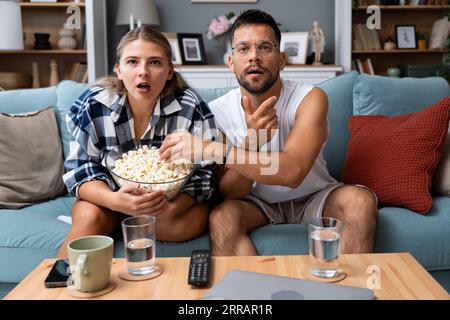 Giovani coppie eccitate e tese sedute sul divano a casa a guardare o guardare eventi sportivi in tv insieme. Uomo e donna guardano una partita di football o di calcio Foto Stock