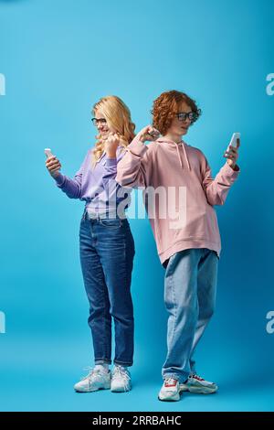 amici adolescenti felici e alla moda con occhiali da vista e con smartphone e con gesto vincente in blu Foto Stock