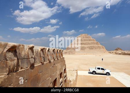 210914 -- SAQQARA, 14 settembre 2021 -- la foto mostra teste di cobra decorate sul muro di edifici in pietra al livello superiore della tomba sud del re Djoser con la piramide a gradoni in lontananza nella necropoli di Saqqara, a sud del Cairo, Egitto, il 14 settembre 2021. L'Egitto il lunedì ha aperto la tomba meridionale del re Djoser dopo il restauro nella necropoli di Saqqara vicino alla capitale il Cairo. Il processo di restauro è iniziato nel 2006 e ha comportato lavori di conservazione e restauro dei corridoi inferiori, rafforzando le pareti e i soffitti, completare le iscrizioni interne nella tomba come riassemblaggio della sa granitica Foto Stock