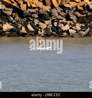 Donna in bikini paddle boarding vicino al muro di mare a Jackson's Bay, il giorno più caldo dell'anno di Barry Island - settembre 2023. Foto Stock
