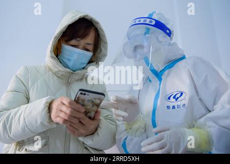 211204 -- MANZHOULI, 4 dicembre 2021 -- Un membro dello staff guida una donna a mostrare il suo codice sanitario su un telefono cellulare in una zona residenziale nella città di confine di Manzhouli nella regione autonoma della Mongolia interna della Cina settentrionale, 4 dicembre 2021. La città di confine di Manzhouli, nella regione autonoma della Mongolia interna della Cina settentrionale, ha riferito 17 casi confermati di COVID-19 trasmessi localmente dalle 12:00 alle 14:00, sabato, hanno dichiarato le autorità locali. Nell'ultima epidemia, la città ha segnalato 314 casi confermati di COVID-19 trasmessi localmente, di cui nove gravi. Team medici esperti hanno preparato programmi di trattamento per Foto Stock