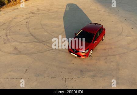 Izmir, Turchia - 2 agosto 2023: Vista droni di una Renault Clio 5 rossa su calcestruzzo con segni di deriva. Le calde tonalità del tramonto mettono in risalto l'ombra dell'auto Foto Stock