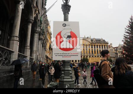 211227 -- BRUXELLES, 27 dicembre 2021 -- le persone camminano davanti a un poster con l'obbligo di indossare maschere per il viso nella Grand Place di Bruxelles, Belgio, il 27 dicembre 2021. Il Belgio ha imposto misure supplementari per rallentare la diffusione della variante Omicron, che sta causando un picco in alcuni casi in tutta Europa. Dal dicembre 26, i mercatini di Natale al coperto, i cinema, i teatri e le sale da concerto sono chiusi, ma i musei e le biblioteche rimangono aperti. BELGIO-BRUXELLES-COVID-19-MEASURES ZhengxHuansong PUBLICATIONxNOTxINxCHN Foto Stock