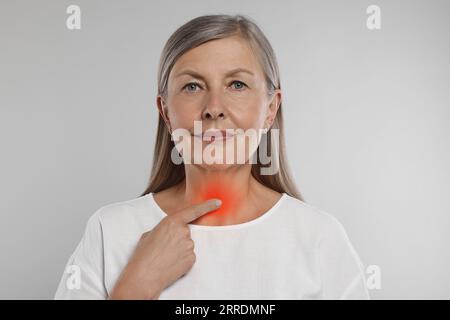 Sistema endocrino. Donna anziana che fa autoesame della tiroide su sfondo grigio chiaro Foto Stock