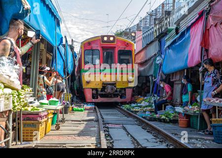 Thailandia, Zugstrecke durch Maeklong Markt in Samut Songkhram 220106 -- BANGKOK, 6 gennaio 2022 -- Un treno pendolare attraversa il mercato ferroviario di Maeklong nella provincia di Samut Songkhram, Thailandia, 5 gennaio 2022. Nel mercato ferroviario di Maeklong, costruito lungo un binario ferroviario, viene raggiunto un compromesso tra i venditori e i treni pendolari di passaggio. Quando il binario della ferrovia è libero, i proprietari di stalle possono allestire le stalle a proprio piacimento. Prima della pandemia di COVID-19, il mercato aveva attirato molti turisti. Oggi, a causa della diminuzione dei passeggeri, il numero di treni che qui ogni giorno navetta è stato ridotto da otto a TW Foto Stock