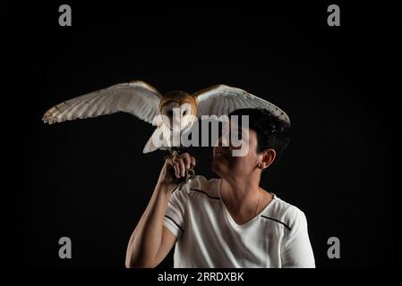 Foto in studio di un bellissimo gufo con le ali allungate e tenute da una donna. Animale selvatico. Isolato su sfondo nero. Foto Stock