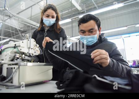 220116 -- YUTIAN, 16 gennaio 2022 -- Maynurhan Amang L insegna Abudulezizi Maisedi cucendo abilità nella fabbrica di Erke nel parco industriale di Tianjin nella contea di Yutian, nella regione autonoma di Xinjiang Uygur, nella Cina nordoccidentale, 13 gennaio 2022. La contea di Yutian, un tempo un'area povera dello Xinjiang, ha intensificato lo sviluppo delle industrie ad alta intensità di lavoro, tra cui tessile, abbigliamento e calzini. Nel parco industriale di Tianjin a Yutian, una base produttiva del marchio sportivo cinese Erke è stata messa in funzione il 1° gennaio 2022, offrendo più di 500 posti di lavoro per la gente del posto. Maynurhan Amang e suo marito Abuduleziz Foto Stock