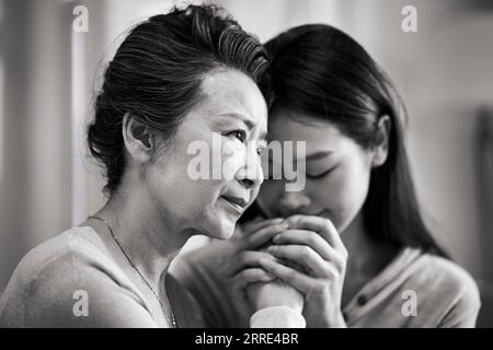 giovane figlia asiatica adulta che consola la madre anziana che vive con malattie mentali, in bianco e nero Foto Stock