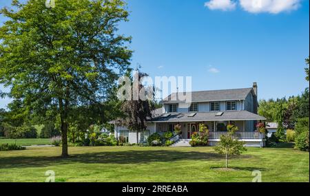 Grande casa di famiglia costruita su terreni agricoli. Immagine di una casa residenziale. Tipica fattoria rurale nordamericana con giardino ben curato in estate Foto Stock