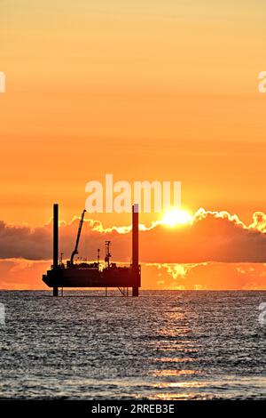 Carro di prova di perforazione ARAN250 jackup con orizzonte dorato cielo arancio nuvoloso e sole che sbircia sopra le nuvole nel Mare del Nord all'alba con cielo caldo Foto Stock