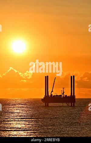 Carro di prova di perforazione ARAN250 jackup con orizzonte dorato cielo arancio nuvole e sole ben sopra le nuvole nel Mare del Nord all'alba con cielo caldo Foto Stock