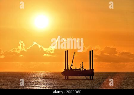 Carro di prova di perforazione ARAN250 jackup con orizzonte dorato cielo arancio nuvole e sole ben sopra le nuvole nel Mare del Nord all'alba con cielo caldo Foto Stock