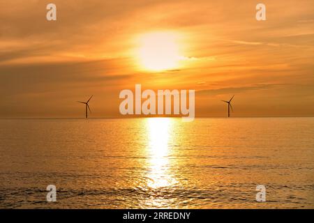 Due turbine eoliche del Mare del Nord al largo della costa di Blyth all'alba con cielo e mare arancioni Foto Stock