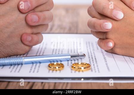 Accoppiare la mano con il divorzio accordo e Golden gli anelli di nozze sulla scrivania in legno Foto Stock