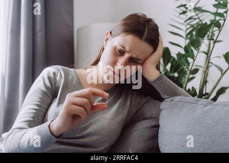Turbata giovane donna caucasica che tiene anello di nozze pensa allo scioglimento del matrimonio o al divorzio che ha problemi familiari. Donna triste infelice stressata con rel Foto Stock
