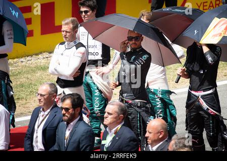 Il campione di F1 Lewis Hamilton indossa la sua tuta da gara, tenendo un ombrello durante un evento pre-gara, incapsulando un momento di calma prima dello stor delle corse Foto Stock