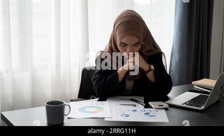 Una donna d'affari musulmana asiatica millenaria e premurosa che indossa un hijab sta esaminando e lavorando sui rapporti d'affari presso la sua scrivania in ufficio. Foto Stock