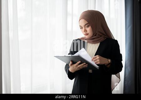 Una donna d'affari musulmana asiatica millenaria, professionale e seria, o una manager donna in un hijab o un velo, sta esaminando i rapporti commerciali mentre è in corso la sua attività Foto Stock