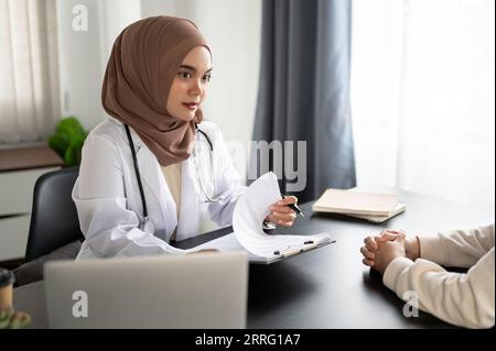 Una bella e professionale medico musulmana asiatica sta consultando un piano chirurgico e un piano di trattamento con un paziente in una sala esame a un hos Foto Stock